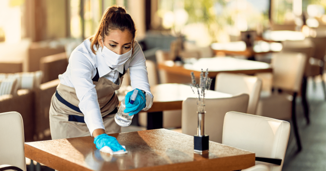 mujer limpiando mesa de restaurante con productos de limpieza especializados para restaurantes